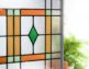 Showing beautiful stained glass window with orange, green, yellow and clear glass with a skewed appearance as to not see clearly through it. The pattern has a dark Christmas green diamond in the middle of the square holding the other colors. The square and recantgular designs are lined in a think black border that makes the colors pop.