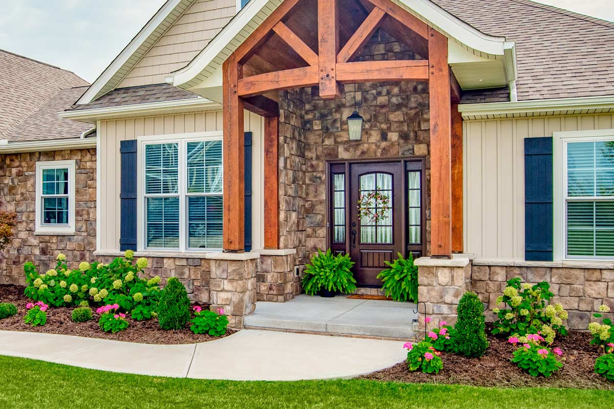 Signet Series ProVia custom doors for your entry with privacy glass and dark wood grain on a beautiful home with stone overlay and creme siding with navy blue shutters on 2 living room windows one on each side of the door.